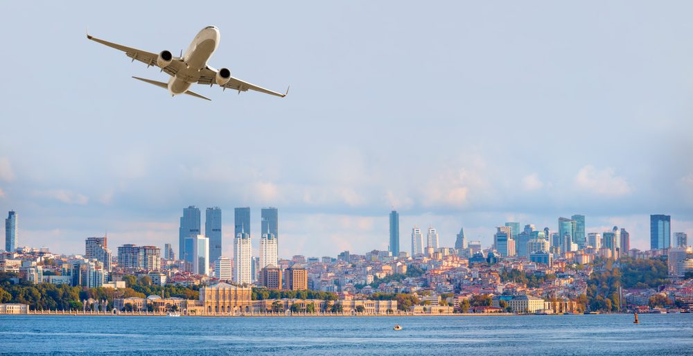 Istanbul skyline across the Bosphorus with modern residential towers and a passenger aircraft flying overhead. 